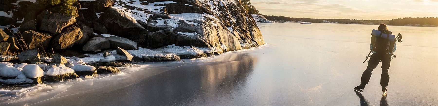 Mies luistelee jäällä kohti auringonlaskua.