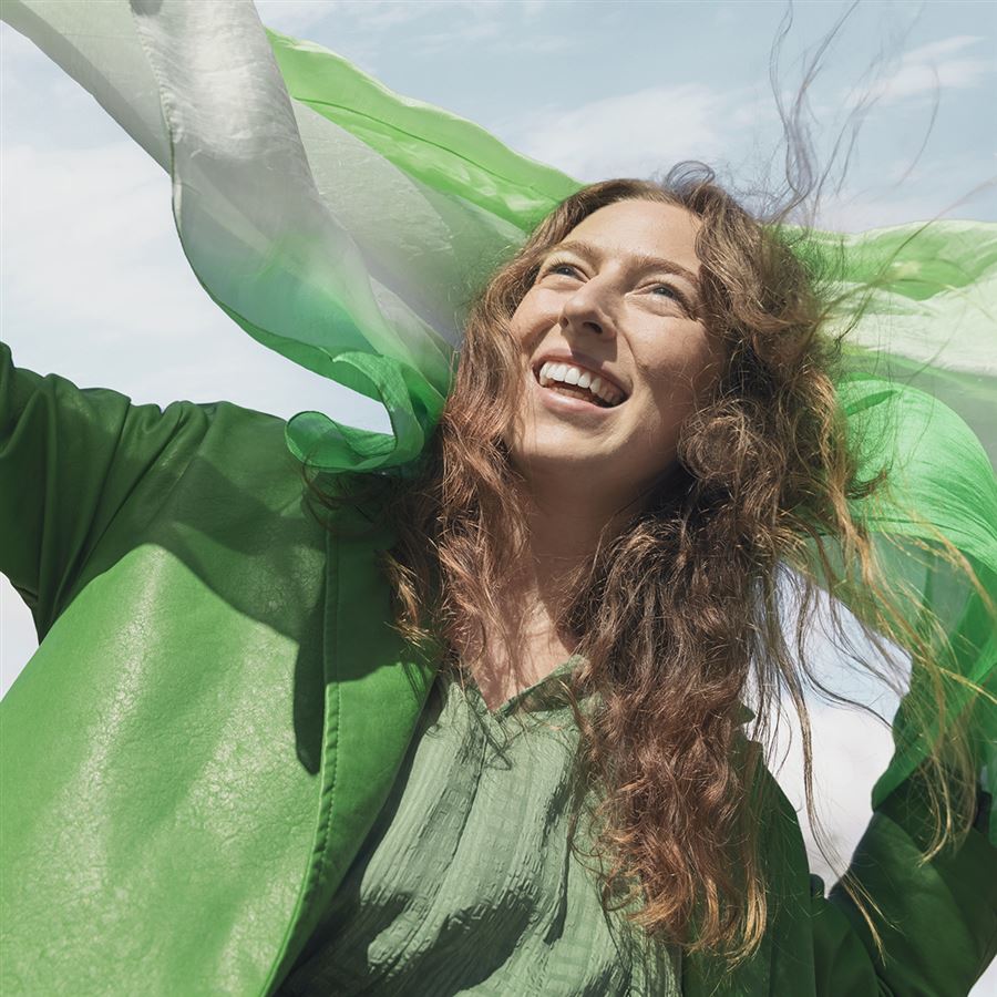 Ung kvinna klädd i grönt som ler i vinden