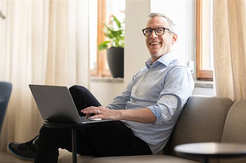 En leende man sitter i soffan med en bärbar dator i knät